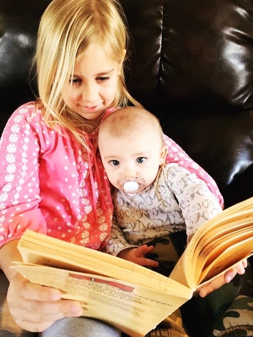 young girl holding a baby in her lap and reading a book kids to read