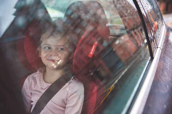 girl looking out car window in booster seat