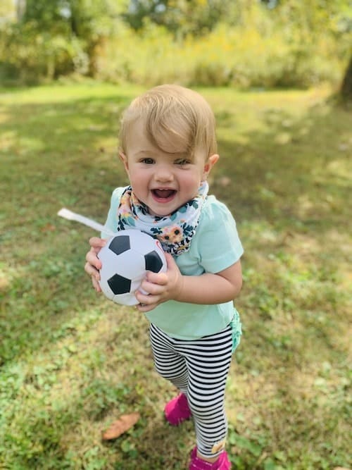 toddler girl holding small ball in backyard choose toys