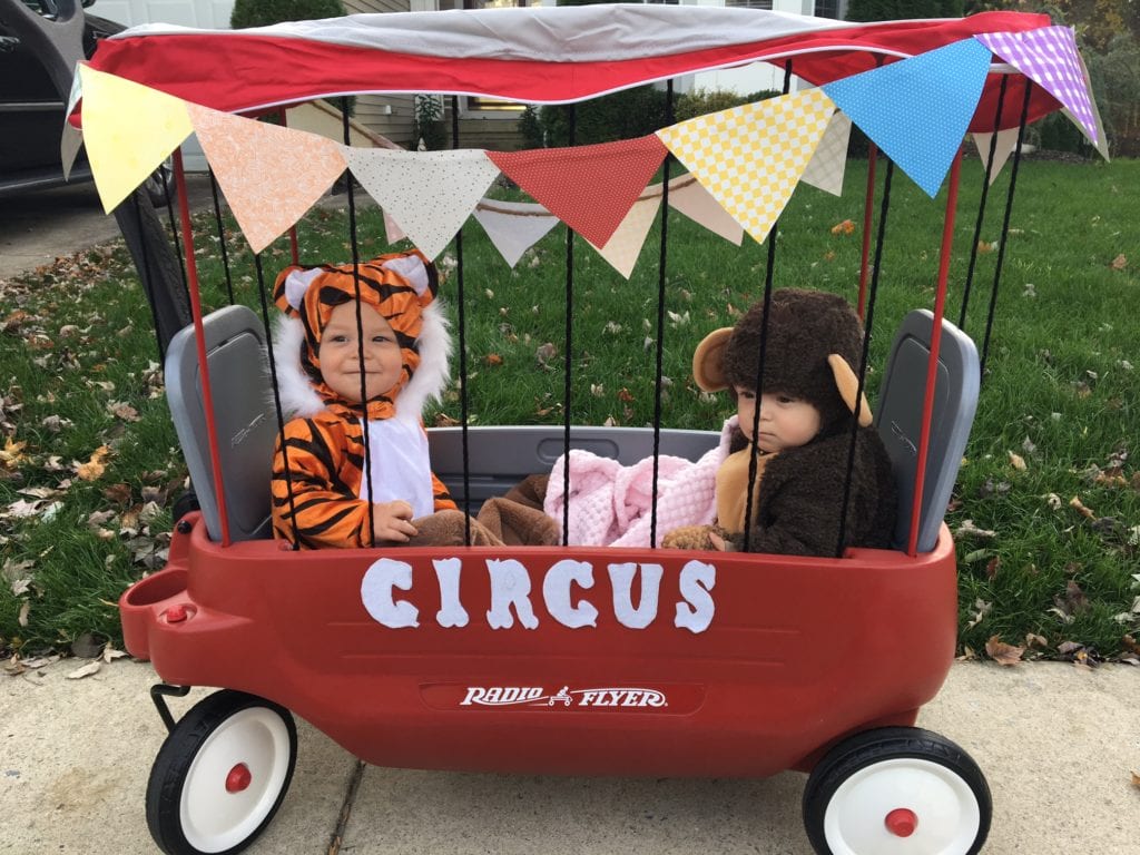 baby twin boys dressed up as a tiger and a monkey in a wagon decorated to look like a cage and it says circus on the side