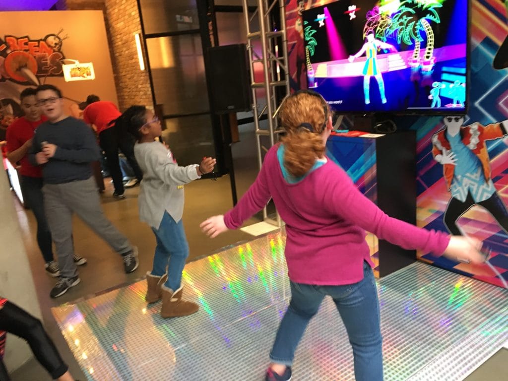 Two girls dancing in front of a TV screen video game