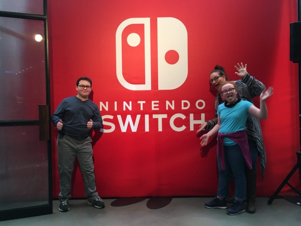 Mom and teen twins at Nintendo Switch launch in front of Nintendo step and repeat. 