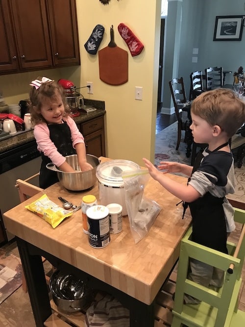 two kids cooking at a high table standing in cooking stools kids cooking