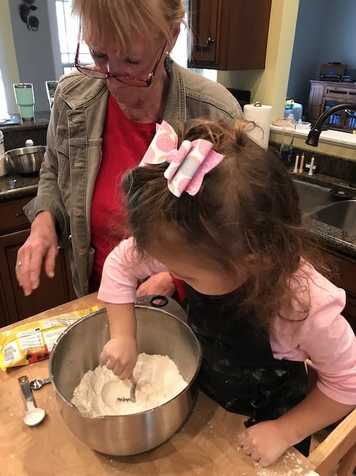 little girl scooping flour and grandma watching kids cooking