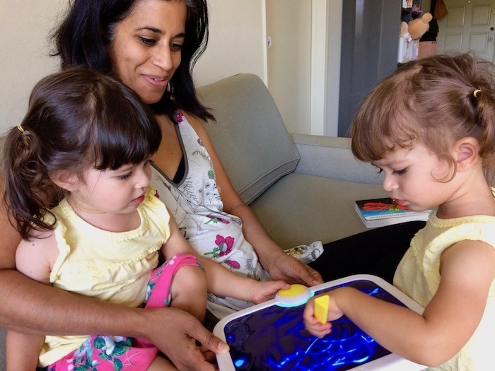 twin girls sitting on mom's lap Sharing Between Twins