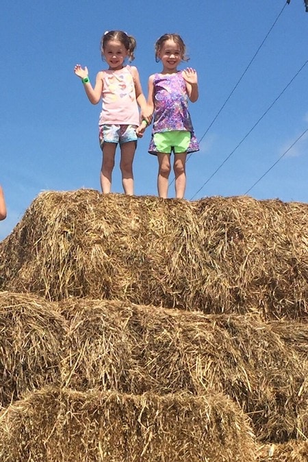 twin girls 5 years old standing on a hay bale embrace their individuality