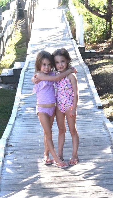 twin girls 5 years old standing on a boardwalk embrace their individuality