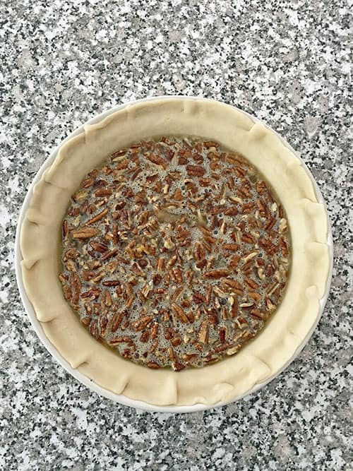 unbaked ingredients in a pie crust to make pecan pie