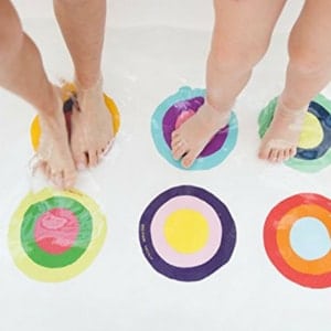 Two pairs of feet standing on a white bath mat with six multicolored circles.