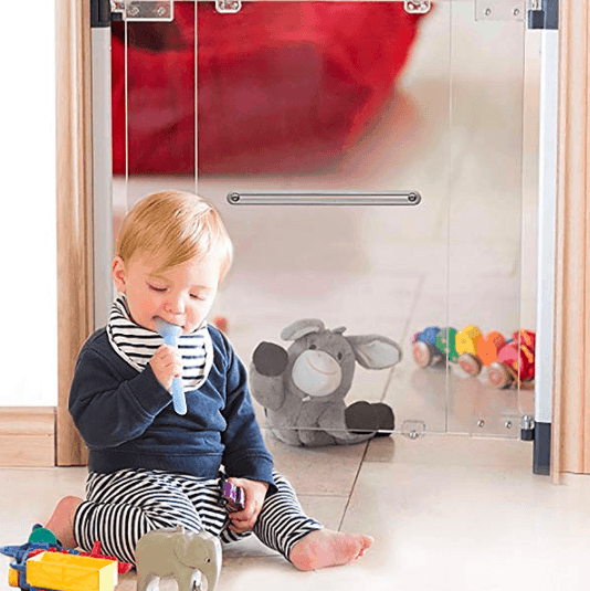 baby with spoon in mouth sitting on the floor in front of clear baby gate baby proofing