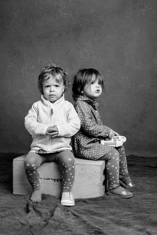 twin toddlers sitting on a box in black and white