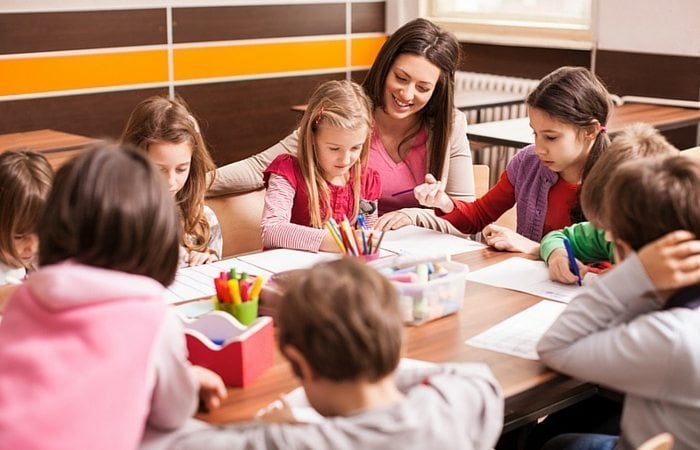 a woman sitting with a table full of young children as they color and draw