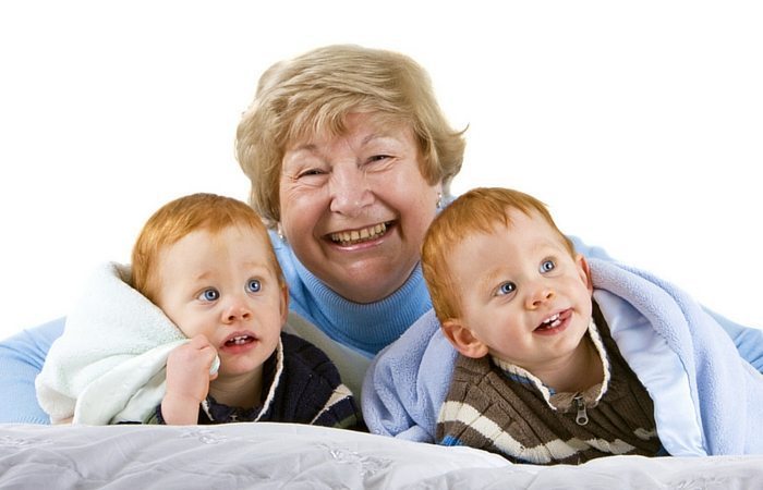 an older woman laying down with young twin boys wrapped in blankets