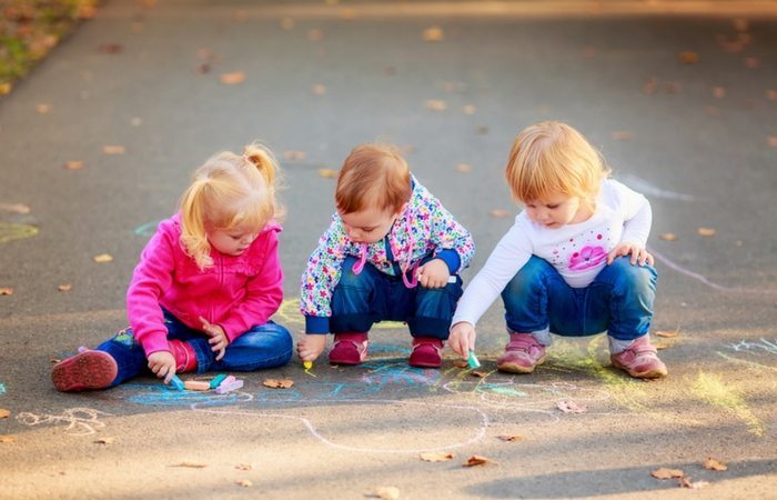 3 toddlers drawing with chalk outisde on sidewalk