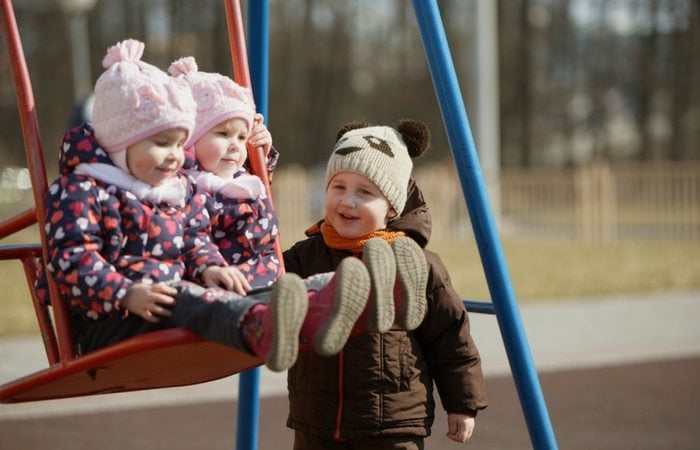 boy pushing twin girls on swing