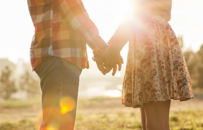 partners holding hand with the sunlight behind them