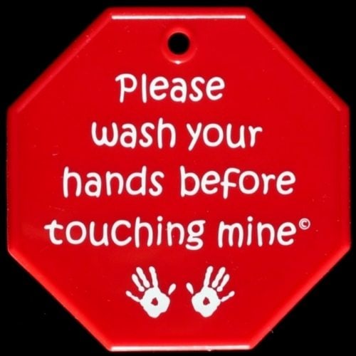 Red sign, shaped like an octagon with white text.  It is created to hang on a stroller, and reads "Please wash your hands before touching mine" with two handprints on the bottom.