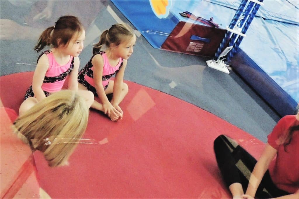 twin girls sitting on mat at gymnastics class after-school activities