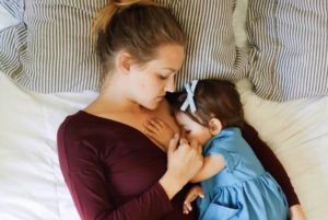 mom breastfeeding a baby lying on a bed feeding twins