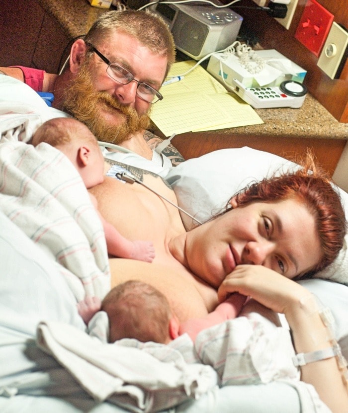 mom breastfeeding twins in the hospital with dad looking on