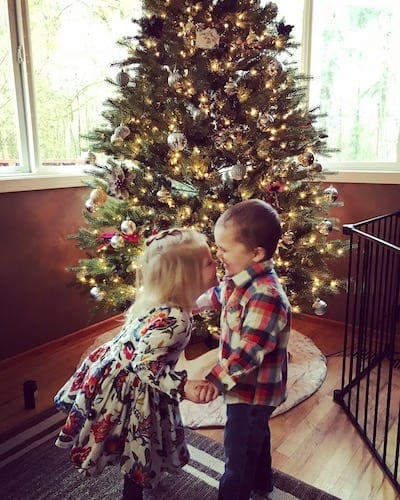 silly questions boy girl toddler twins holding hands, facing each other, and smiling at one another in front of a lit Christmas tree