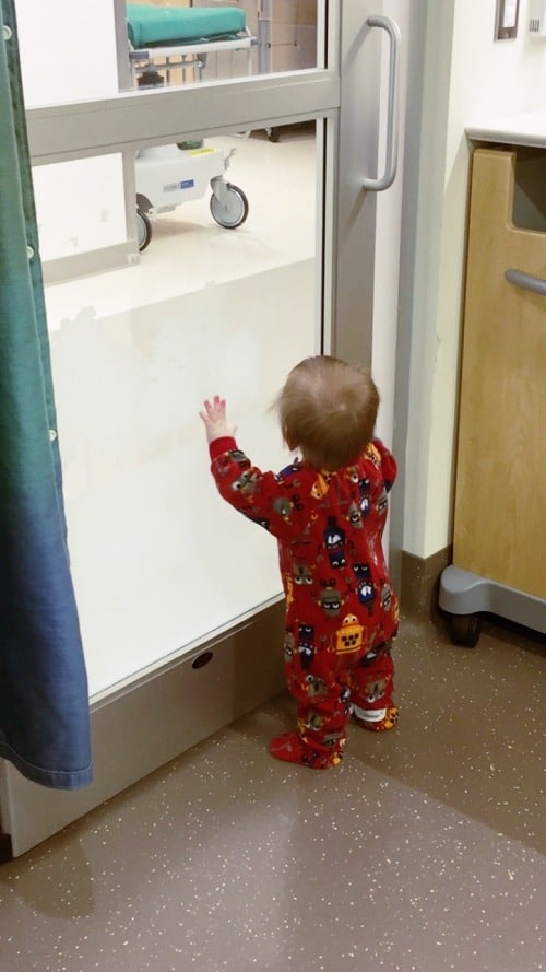 1 year old boy standing at glass door in hospital ear tubes