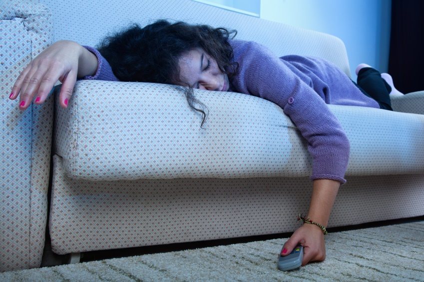 Young woman sleep on the couch in a dark living room with the TV on amd remote in hand. guilt