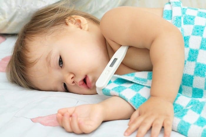 toddler laying down sick with thermometer under her armpit the flu