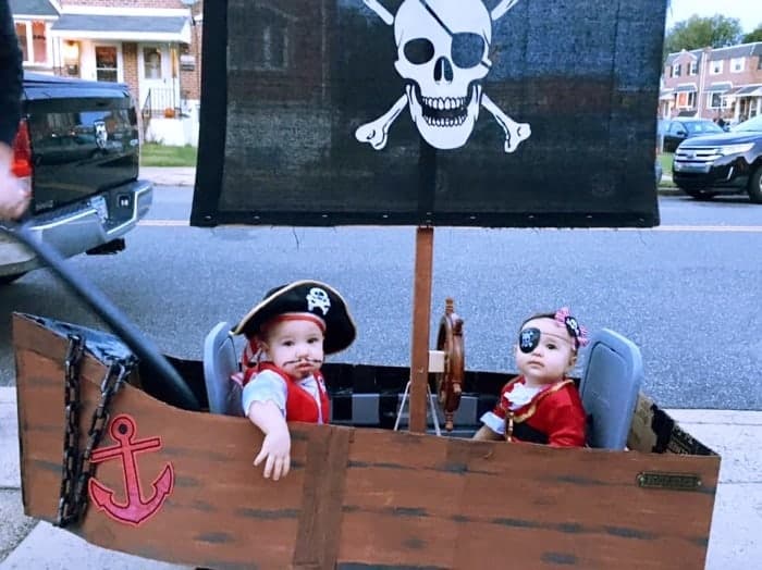 twin babies dressed as pirates sitting in a wagon dressed up as a pirate ship