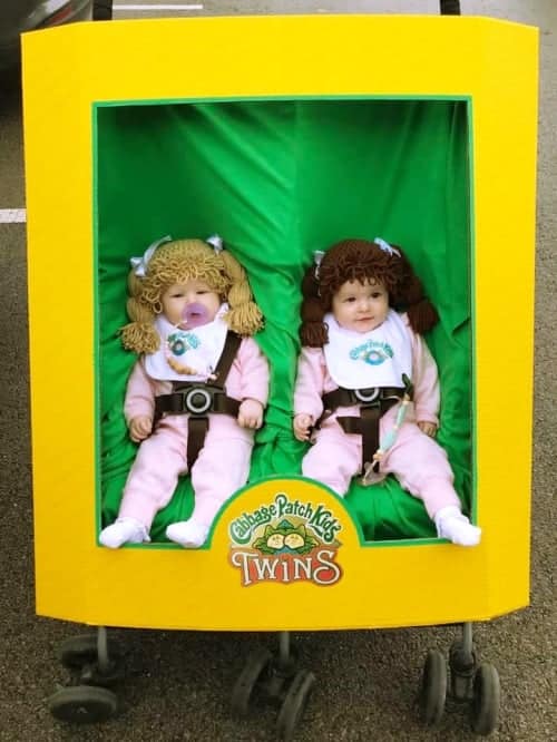 twin baby girls dressed up as cabbage patch kids and sitting in a stroller that's made up to look like a box