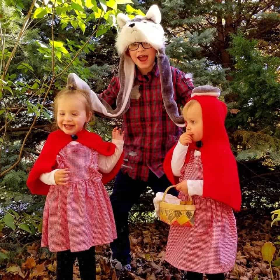 twin toddler girls dressed up as little red riding hood and their older brother dressed up as the wolf in the center