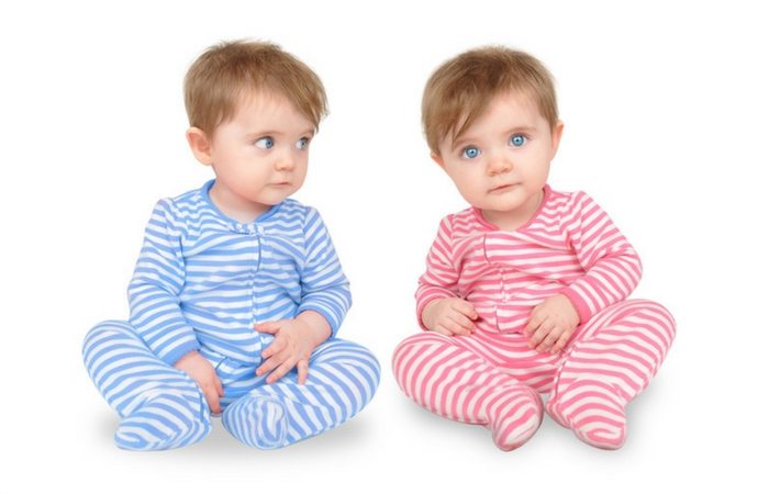 Boy/girl twins sitting up, still in their pajamas. The little boy is wearing blue and white stripped pj's and the little girl is wearing pink and white stripped pj's. 