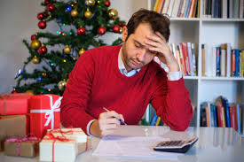 man sitting at a table writing on paper with calculator and christmas tree holiday stress