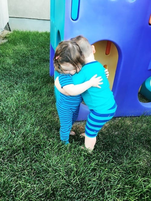 twin toddlers hugging in the back yard look forward