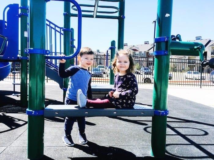 twin toddlers on playground equipment look forward