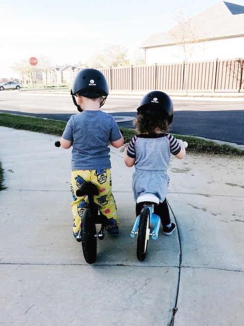 twin toddlers riding balance bikes with helmets look forward