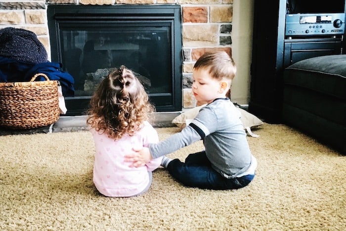 twin toddlers sitting on carpet look forward