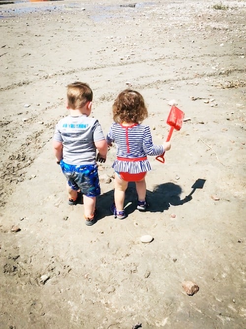 twin toddlers on the beach sand look forward