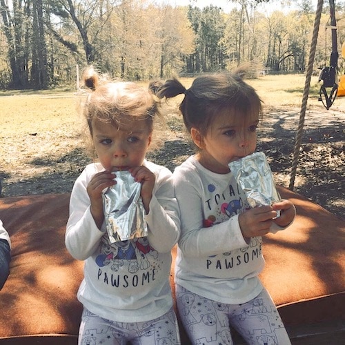 twin girls drinking juice boxes at the park parenting