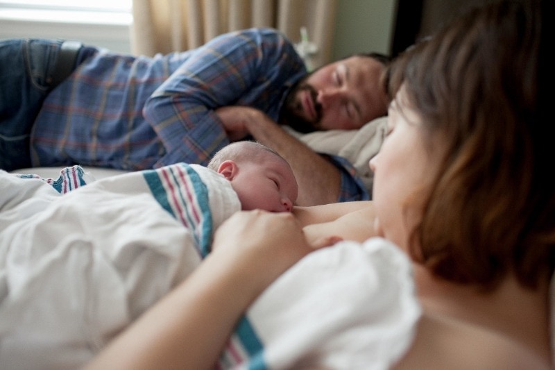 parents in bed with newborn sleep deprived