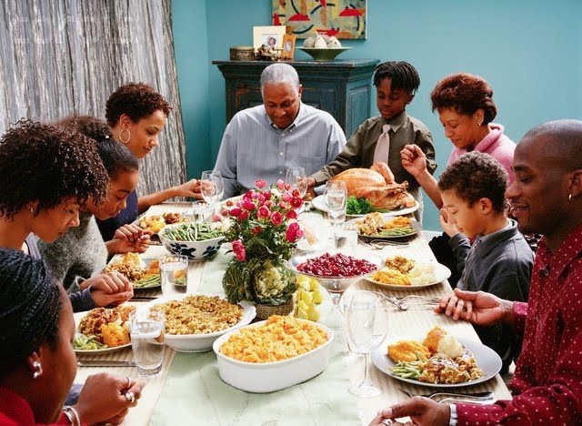 Thanksgiving Dinner family in prayer around a table with a full thanksgiving dinner in front of them
