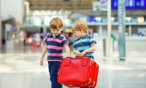 2 young boys in an airport carrying a large suitcase preparing for air travel