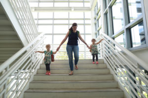 twin toddlers walking down stairs holding mom's hands