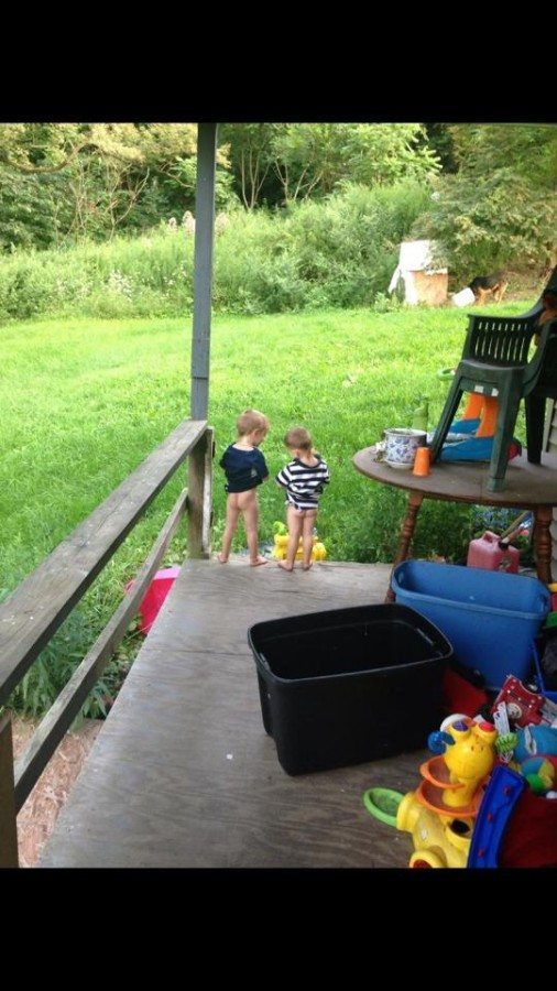 two little boys with no pants, standing on the edge of a porch peeing into the grass at a distance