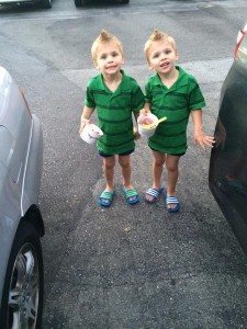 young blonde twins in matching green shirts standing outside between two cars with ice cream