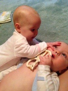 one infant twin climbing on the other on the floor