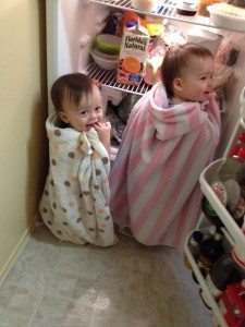 twin toddlers creating mischief wrapped in blankets looking in a refrigerator