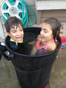 young boy and girl in a tub of water outside with a hose hanging on a wall